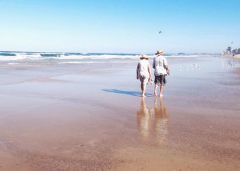 Rear view of senior couple walking at beach against blue sky