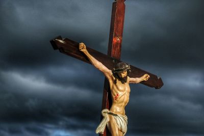 Low angle view of crucifix against cloudy sky