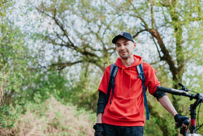 A young man in red hoodie and cap smiling.