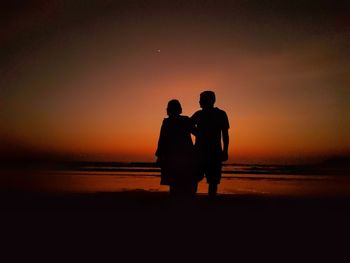 Silhouette men standing on beach against sky during sunset