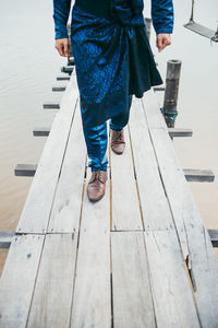 Low section of man walking on pier over sea