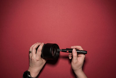 Close-up of person cleaning camera lens against colored background