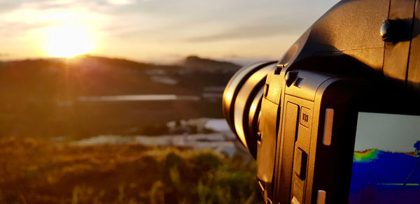 Close-up of camera against sky during sunset