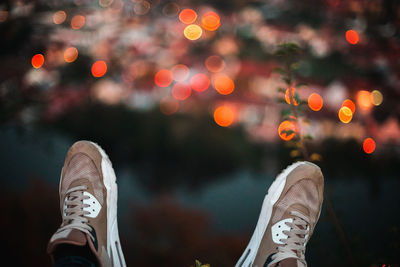 Low section of person wearing shoes against illuminated city during sunset