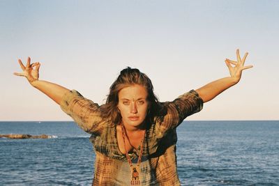 Portrait of woman with arms outstretched at beach against sky