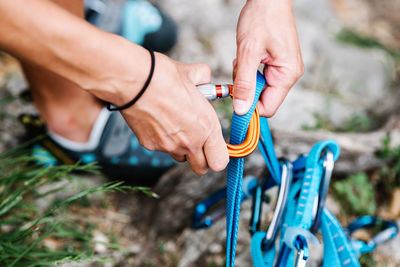 Cropped hands of female hiker attaching belt on carabiner while preparing for climbing