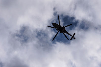 Low angle view of silhouette helicopter against cloudy sky