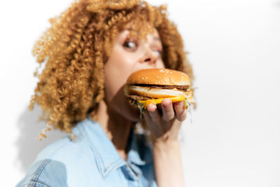 Portrait of smiling young woman holding burger against white background
