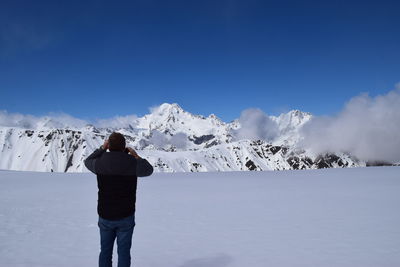 Rear view of person standing on snowcapped mountain against sky