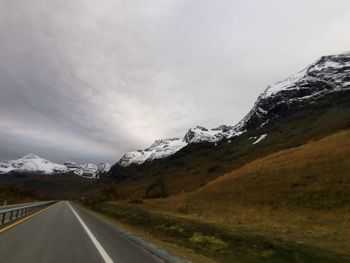 Empty road leading towards mountain range against sky