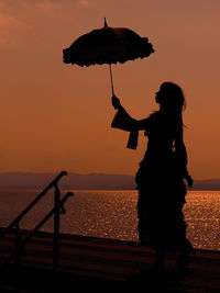 Silhouette woman standing by sea against sky during sunset