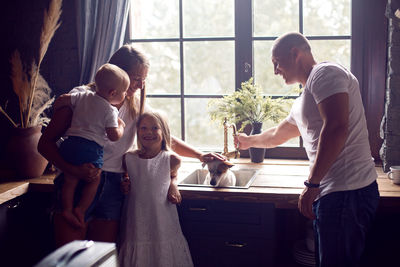 Family with two children and a dog standing in the kitchen by the window