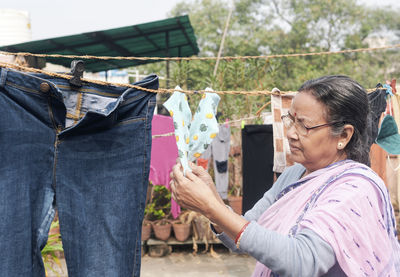 Portrait of a simple looking mature indian woman hanging freshly washed laundry to dry in the sun