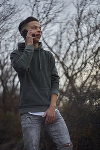 Smiling man talking on mobile phone against bare tree