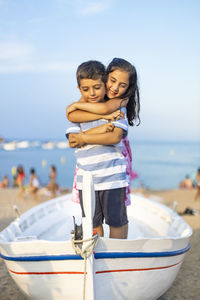 Girl embracing brother while standing in boat at beach