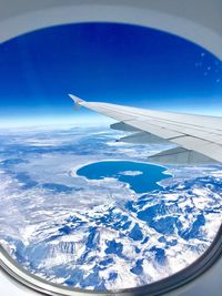 Aerial view of airplane wing over landscape against blue sky
