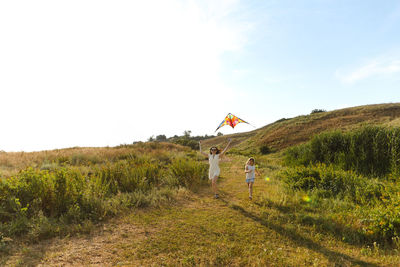Mother holding kite by daughter running on grass against sky
