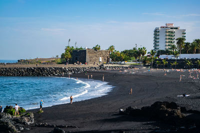 People on beach by buildings against sky in city