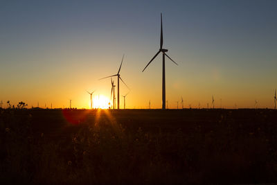 Silhouette windmills on field against orange sky during sunset