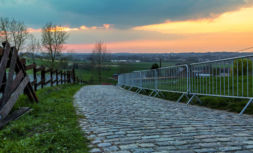 Footpath by railing against sky during sunset