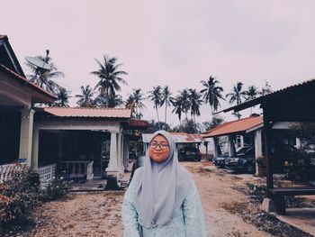 Portrait of smiling young woman standing by palm trees