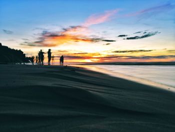 Silhouette people on beach against sky during sunset