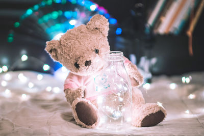 Close-up of teddy bear with bottle and illuminated string light