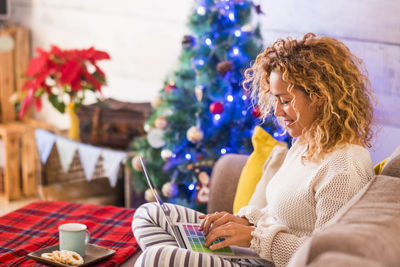 Rear view of woman sitting by christmas tree at home