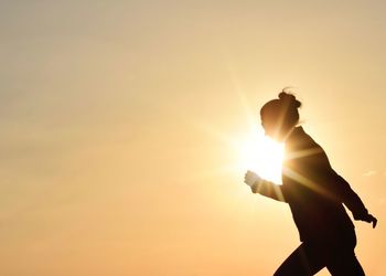 Silhouette boy standing against sky during sunset