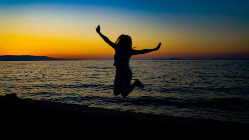 Silhouette woman jumping at beach against sky during sunset