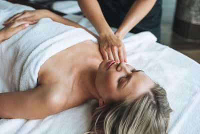 Attractive blonde young woman on couch with white linen enjoys hand facial massage in spa