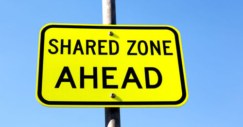 Low angle view of road sign against clear blue sky