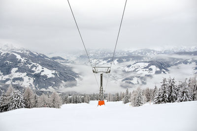 Overhead cable car construction over snowcapped mountains against sky