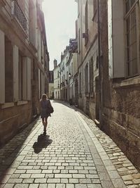 Rear view of woman walking on cobblestone street in city