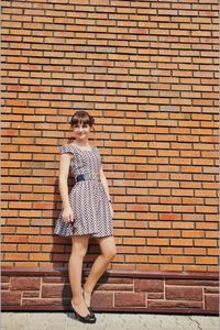 Full length portrait of woman standing against brick wall