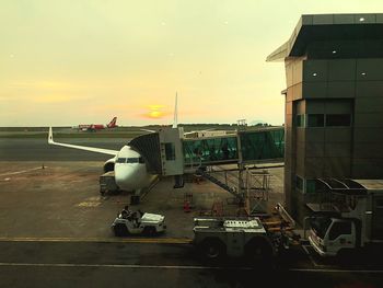 Airplane on airport runway against sky during sunset