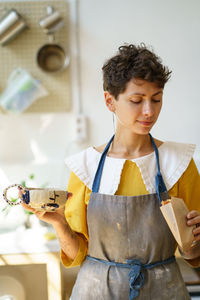 Satisfied young woman ceramist drink coffee from handmade potter cup and has snack in pottery studio