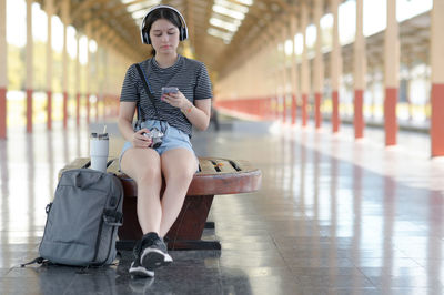 Teenage traveler listening to music with headphones while waiting for the train at platform.