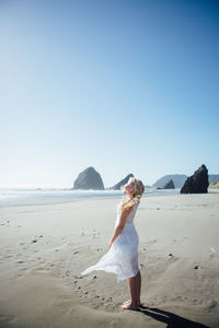 Woman standing on beach against clear blue sky