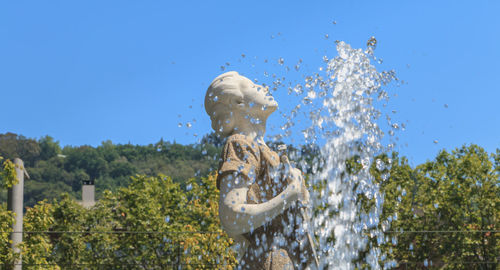 Statue by fountain against clear blue sky