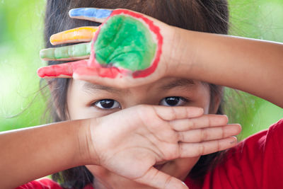 Close-up portrait of girl with colorful paint on hand outdoors