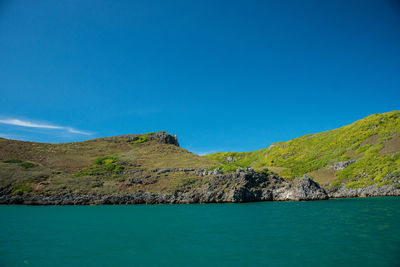 Scenic view of mountains in sea against blue sky