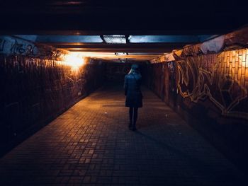 Rear view of woman walking on footpath in illuminated tunnel