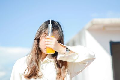 Young woman holding drink while standing against clear blue sky during sunny day