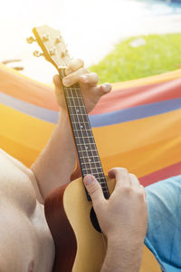 Midsection of man playing guitar while sitting in hammock