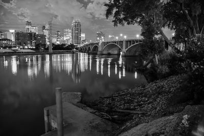 Bridge over river by buildings against sky at night