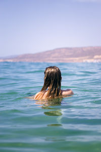 Rear view of woman swimming in sea against clear sky