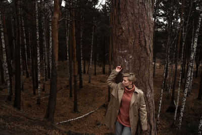 Young woman standing by tree trunk in forest