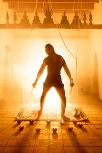 Full length of shirtless man standing against illuminated orange sky