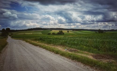 Dirt road amidst field against sky